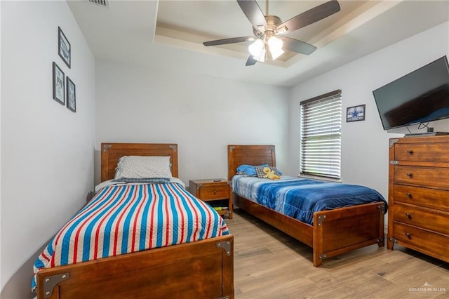 bedroom with a tray ceiling, ceiling fan, wood finished floors, and visible vents