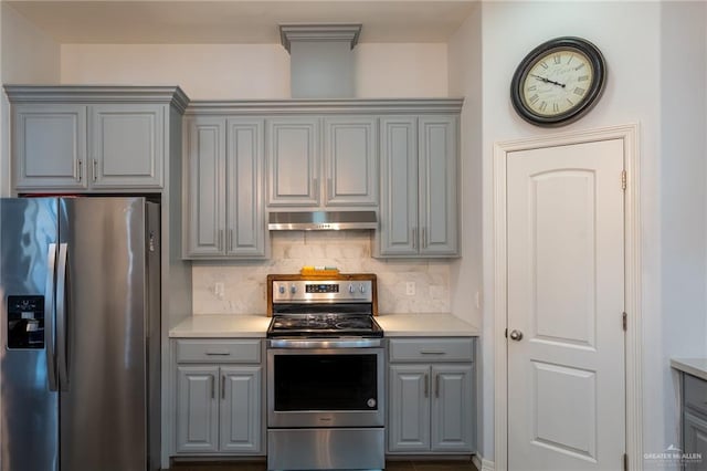 kitchen featuring decorative backsplash, light countertops, under cabinet range hood, appliances with stainless steel finishes, and gray cabinetry