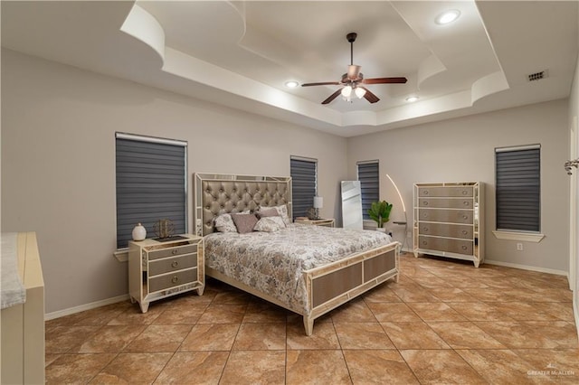 bedroom featuring light tile patterned floors, a ceiling fan, visible vents, baseboards, and a raised ceiling