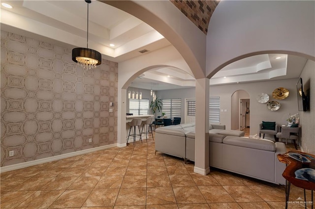 living area featuring light tile patterned flooring, an accent wall, visible vents, baseboards, and a tray ceiling