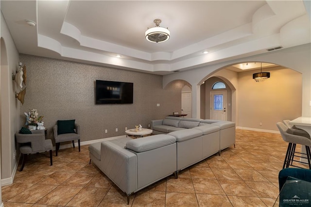 living area with arched walkways, light tile patterned floors, visible vents, baseboards, and a tray ceiling