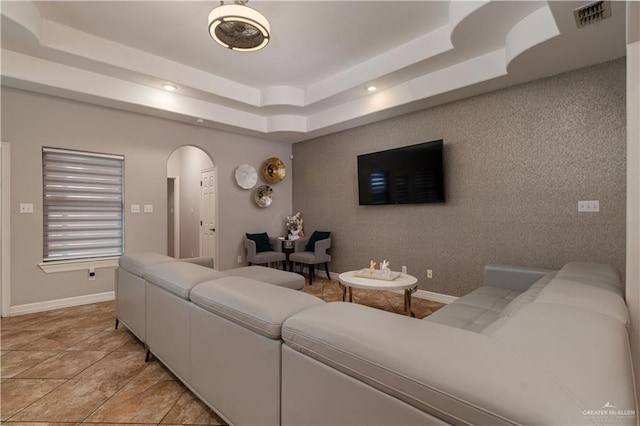 living area featuring arched walkways, recessed lighting, visible vents, baseboards, and a raised ceiling