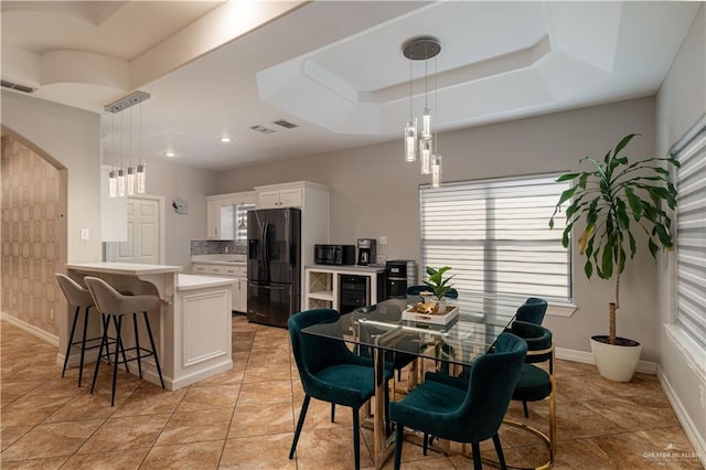 dining space featuring baseboards, visible vents, arched walkways, and a tray ceiling