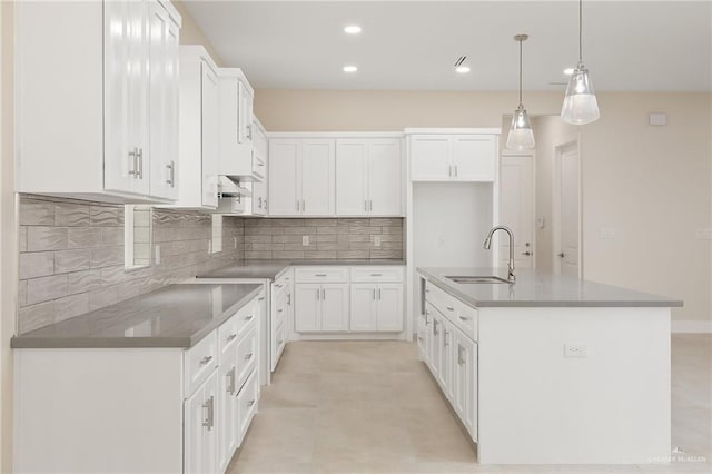 kitchen with an island with sink, sink, hanging light fixtures, and white cabinets