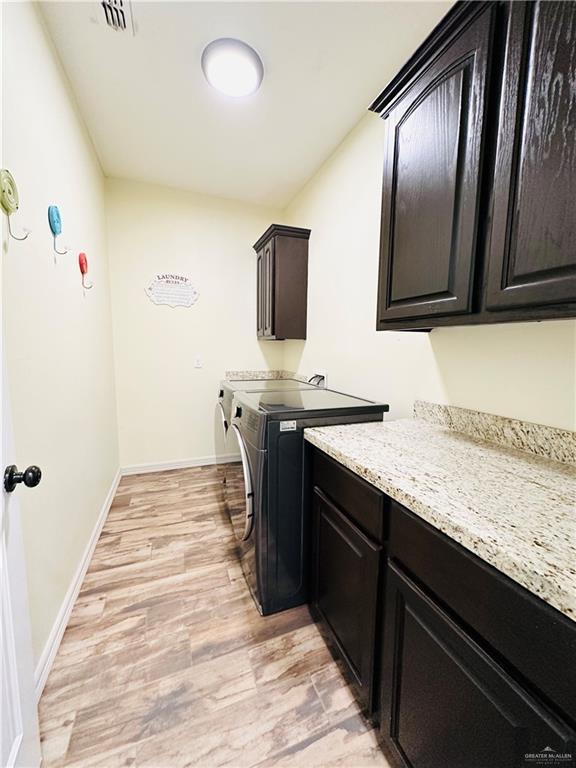 washroom featuring separate washer and dryer, visible vents, baseboards, cabinet space, and light wood finished floors