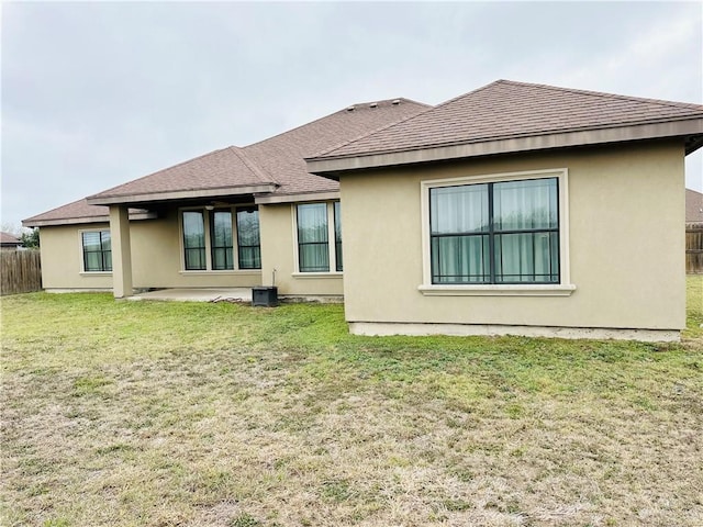 rear view of property featuring a patio, fence, roof with shingles, a lawn, and stucco siding