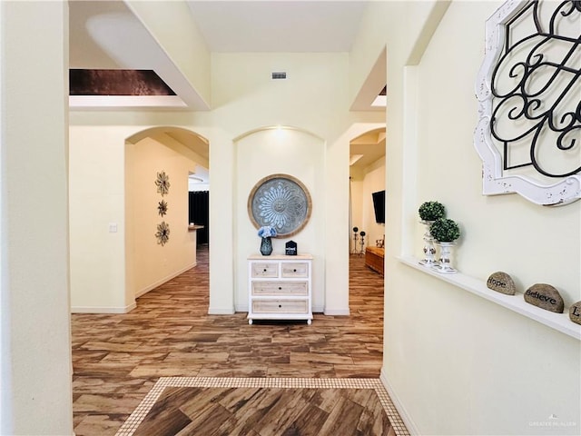 hallway with arched walkways, visible vents, baseboards, and wood finished floors