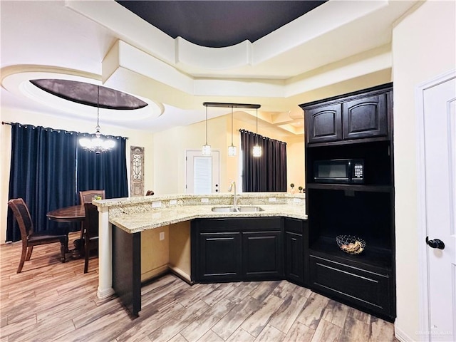 kitchen featuring light wood-type flooring, a tray ceiling, black microwave, and a sink