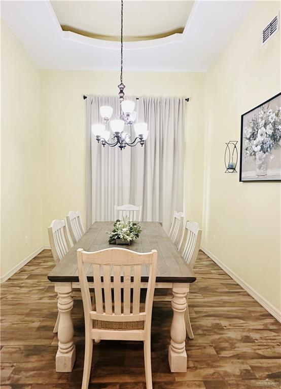 dining area featuring a raised ceiling, visible vents, baseboards, and wood finished floors