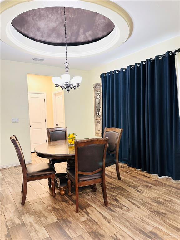 dining area with light wood-style flooring, visible vents, a tray ceiling, and a notable chandelier