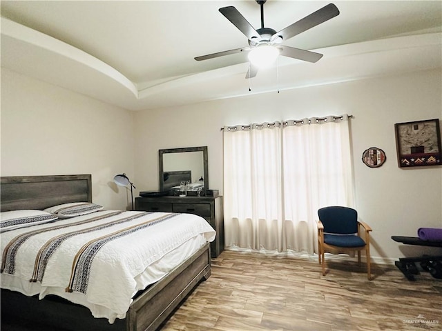 bedroom featuring ceiling fan, a tray ceiling, and light wood finished floors