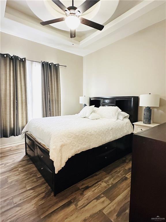 bedroom with dark wood-style flooring, a raised ceiling, and a ceiling fan