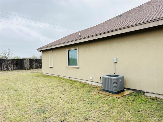 view of property exterior featuring fence, central AC unit, a lawn, and roof with shingles