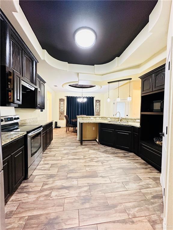 kitchen featuring a tray ceiling, pendant lighting, stainless steel electric stove, a sink, and dark brown cabinets