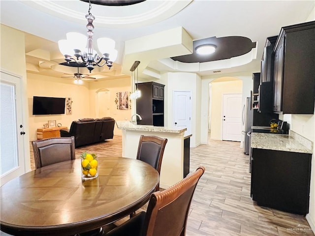 dining room featuring a tray ceiling, wood finish floors, arched walkways, and ceiling fan with notable chandelier