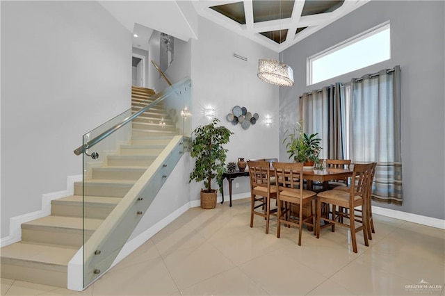 tiled dining space featuring baseboards, a high ceiling, stairway, and coffered ceiling