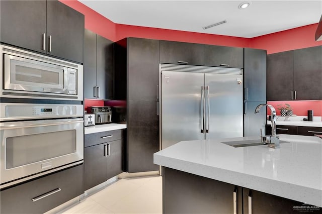 kitchen featuring visible vents, light stone counters, a sink, and built in appliances