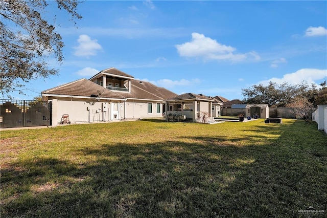 back of house with a lawn, a fenced backyard, an outbuilding, a storage unit, and stucco siding