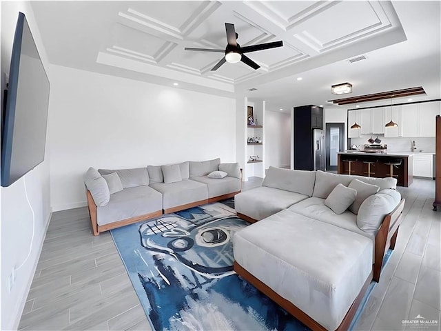 living room featuring ceiling fan, sink, built in shelves, and coffered ceiling