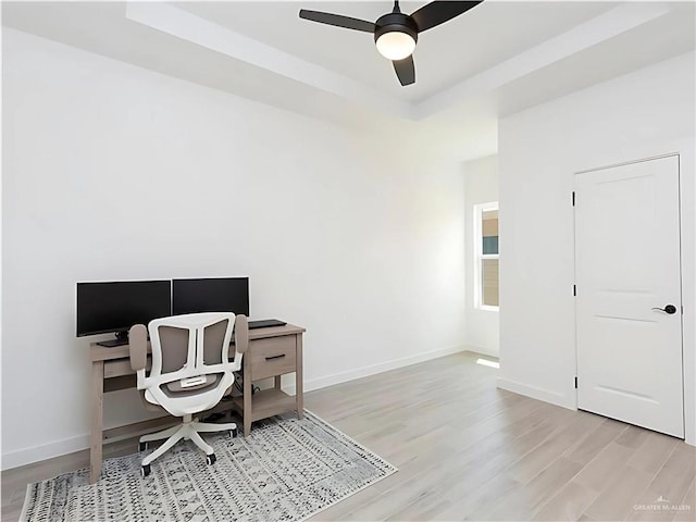 home office with light wood-type flooring, a tray ceiling, and ceiling fan