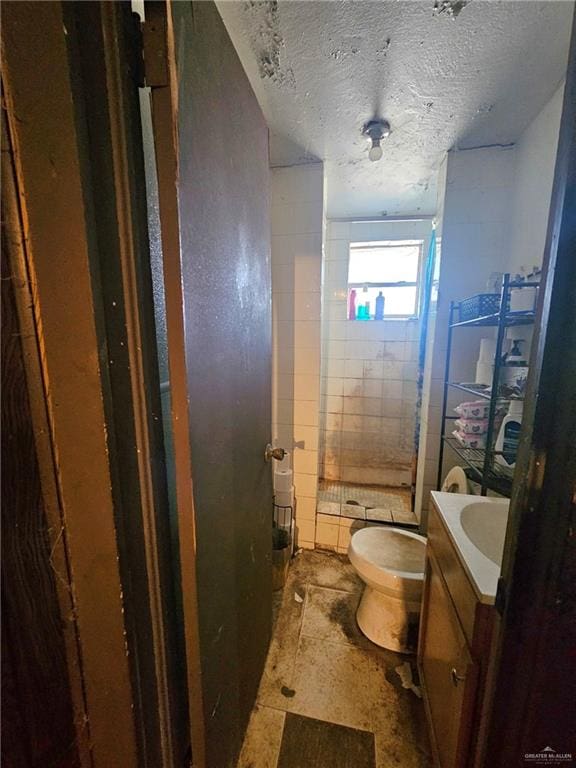 bathroom featuring tiled shower, a textured ceiling, vanity, and toilet