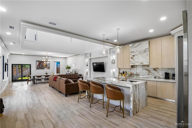 kitchen with light stone counters, a kitchen bar, light brown cabinetry, a center island with sink, and light wood-type flooring