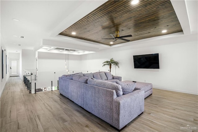 living room with light wood-type flooring, a tray ceiling, and ceiling fan