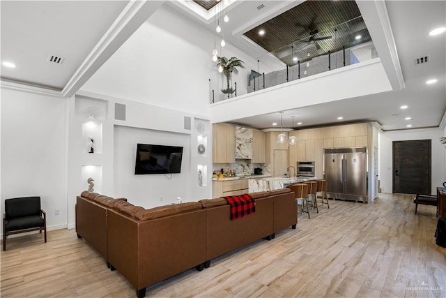 living room with ceiling fan, a towering ceiling, and light wood-type flooring