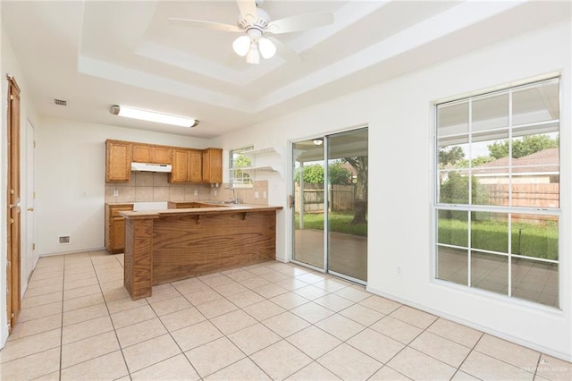 kitchen with kitchen peninsula, backsplash, a tray ceiling, and ceiling fan