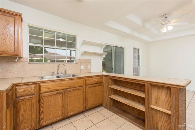 kitchen with kitchen peninsula, decorative backsplash, tile countertops, and sink