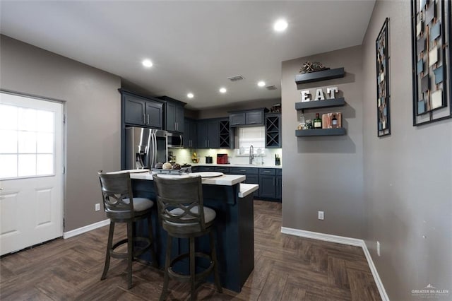 kitchen with dark parquet flooring, stainless steel appliances, a kitchen breakfast bar, and a center island