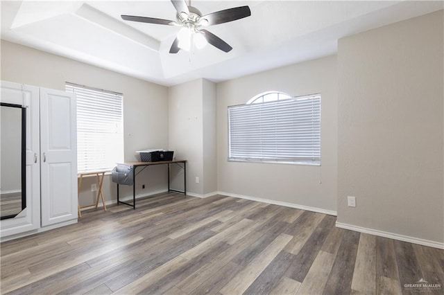 unfurnished office featuring a raised ceiling, ceiling fan, and hardwood / wood-style floors