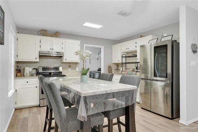 1103 Sun Valley St, San Juan, TX 78589 - kitchen with stainless steel appliances, under cabinet range hood, light wood-style flooring, white cabinets, and tasteful backsplash
