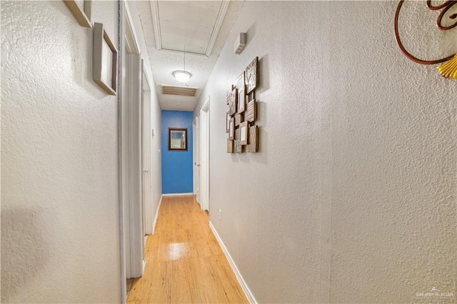 hall featuring light wood-type flooring, attic access, baseboards, and a textured wall