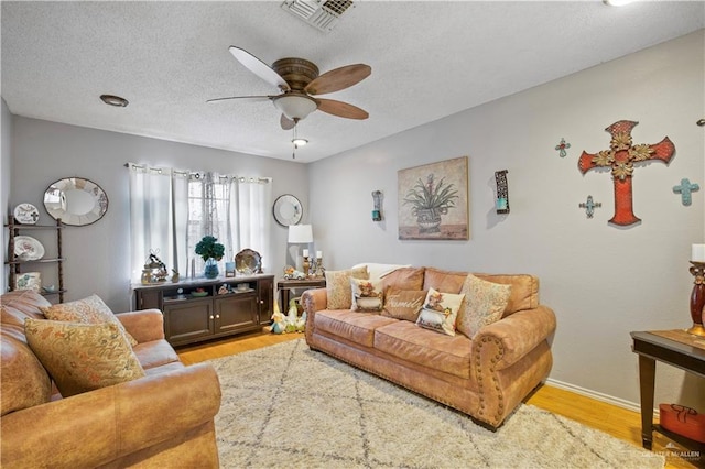 living area featuring light wood finished floors, ceiling fan, visible vents, and a textured ceiling