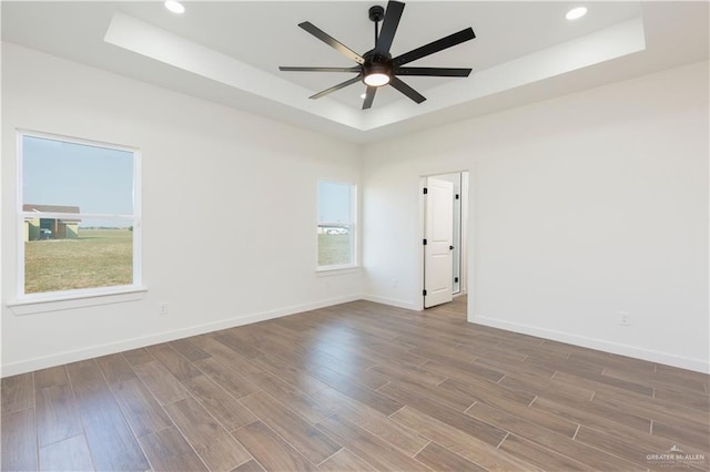 empty room with hardwood / wood-style floors, a raised ceiling, and ceiling fan