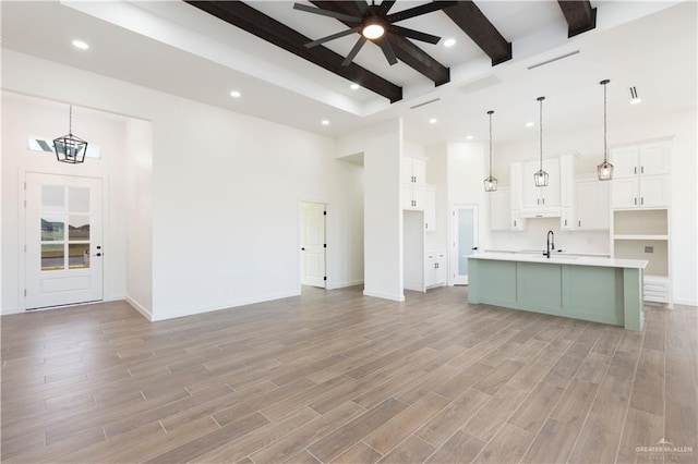 unfurnished living room with beamed ceiling, a towering ceiling, ceiling fan with notable chandelier, and light hardwood / wood-style floors