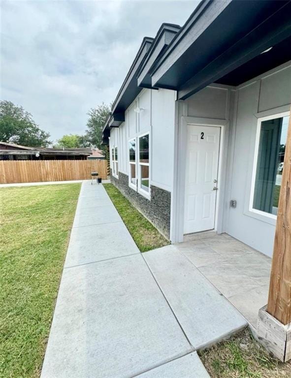 view of side of home with a patio, a yard, fence, and stucco siding