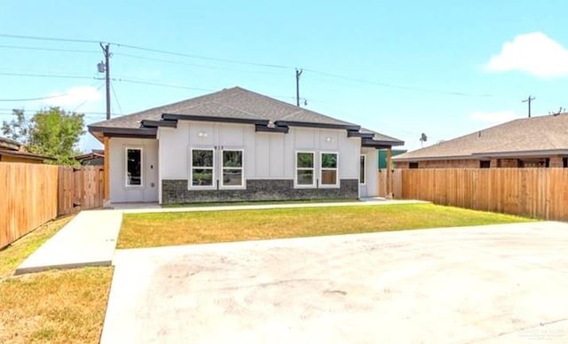 view of front of property featuring board and batten siding, a fenced backyard, and a front lawn