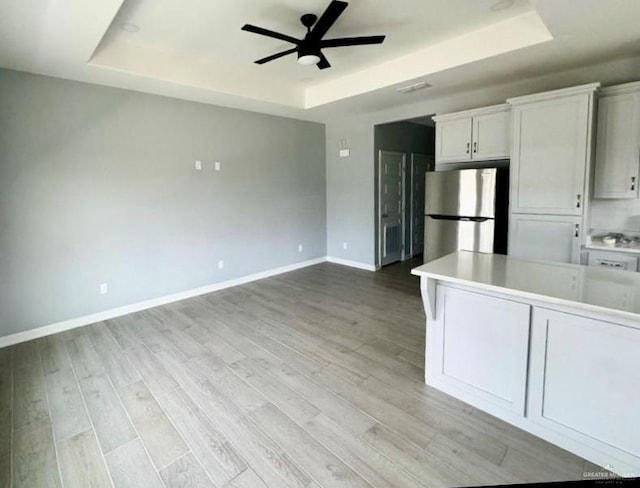 kitchen featuring a raised ceiling, light countertops, freestanding refrigerator, white cabinets, and baseboards