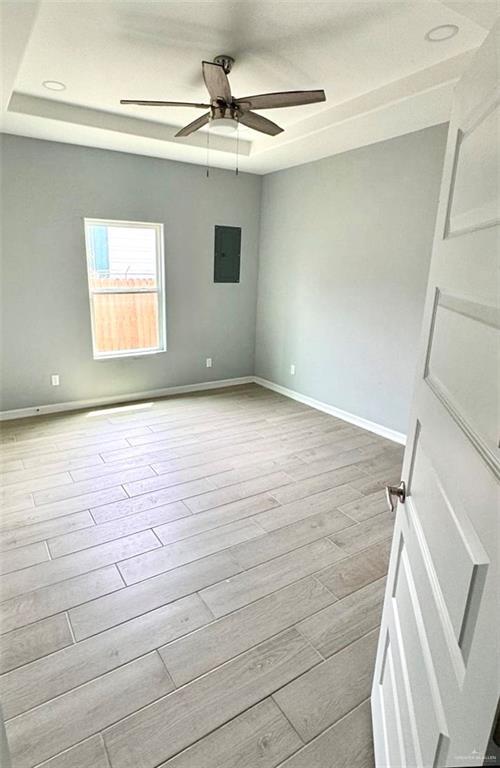 unfurnished room with electric panel, baseboards, a raised ceiling, a ceiling fan, and light wood-type flooring