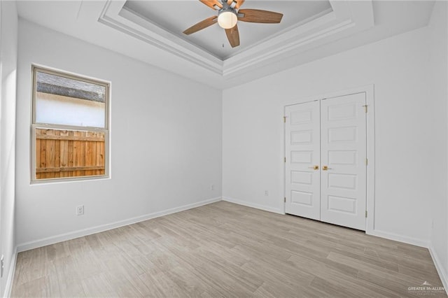 empty room featuring a tray ceiling, ceiling fan, and light hardwood / wood-style floors