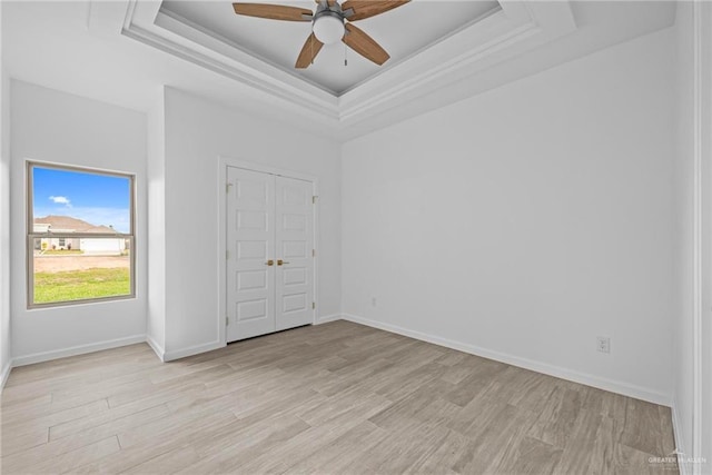 unfurnished bedroom featuring ceiling fan, a raised ceiling, light hardwood / wood-style flooring, and a closet