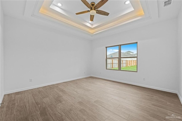 unfurnished room featuring ceiling fan, a raised ceiling, and light wood-type flooring