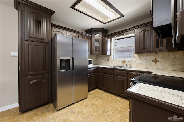 kitchen featuring appliances with stainless steel finishes, glass insert cabinets, dark brown cabinets, and tasteful backsplash