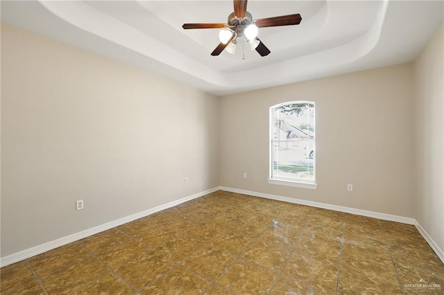 unfurnished room with ceiling fan, a tray ceiling, and baseboards