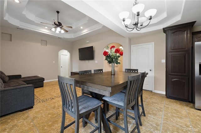 dining room with arched walkways, a raised ceiling, and baseboards