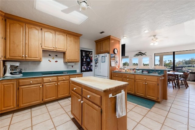 kitchen with a center island, white refrigerator, black cooktop, decorative backsplash, and light tile patterned floors