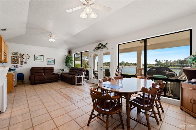 tiled dining space featuring french doors, a water view, vaulted ceiling, and ceiling fan