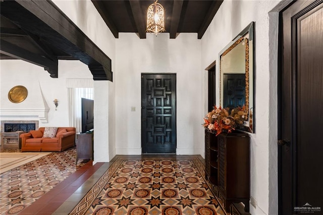 tiled foyer entrance featuring beam ceiling, a large fireplace, and an inviting chandelier